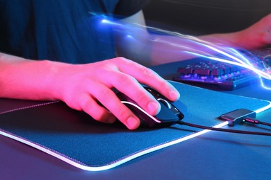 Photo of Gamer using modern wired computer mouse in neon lights at dark table, closeup