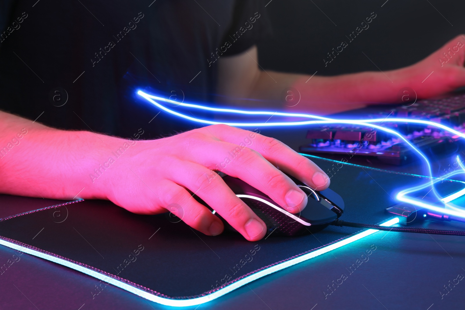 Photo of Gamer using modern wired computer mouse in neon lights at dark table, closeup