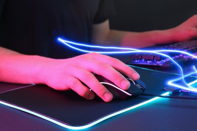 Photo of Gamer using modern wired computer mouse in neon lights at dark table, closeup