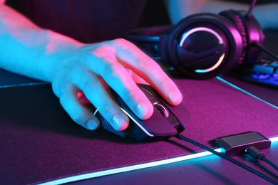 Photo of Gamer using modern wired computer mouse in neon lights at dark table, closeup