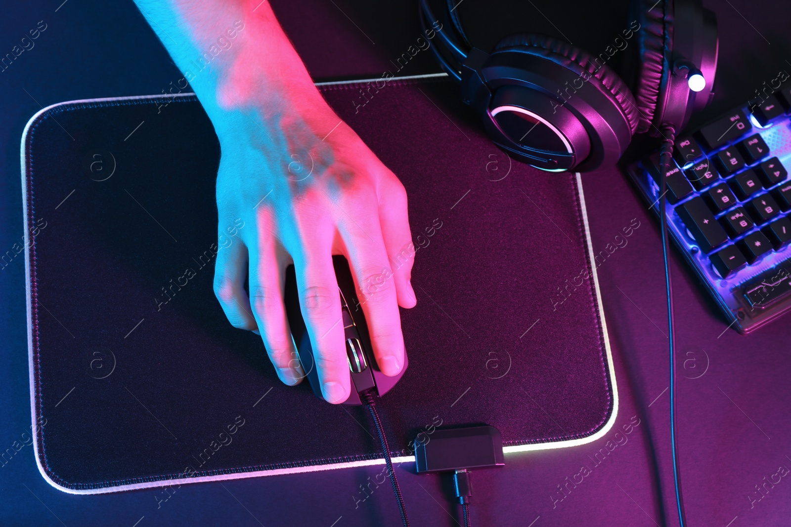 Photo of Gamer using modern wired computer mouse at dark table in neon lights, top view