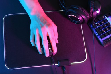 Photo of Gamer using modern wired computer mouse at dark table in neon lights, top view