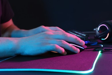 Photo of Gamer using modern wired computer mouse in neon lights at dark table, closeup