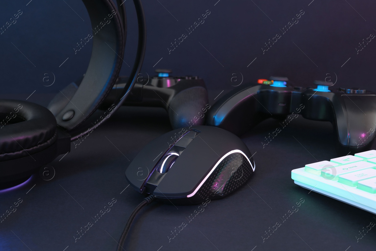 Photo of Computer mouse, headset, RGB keyboard and game controllers on black background, closeup