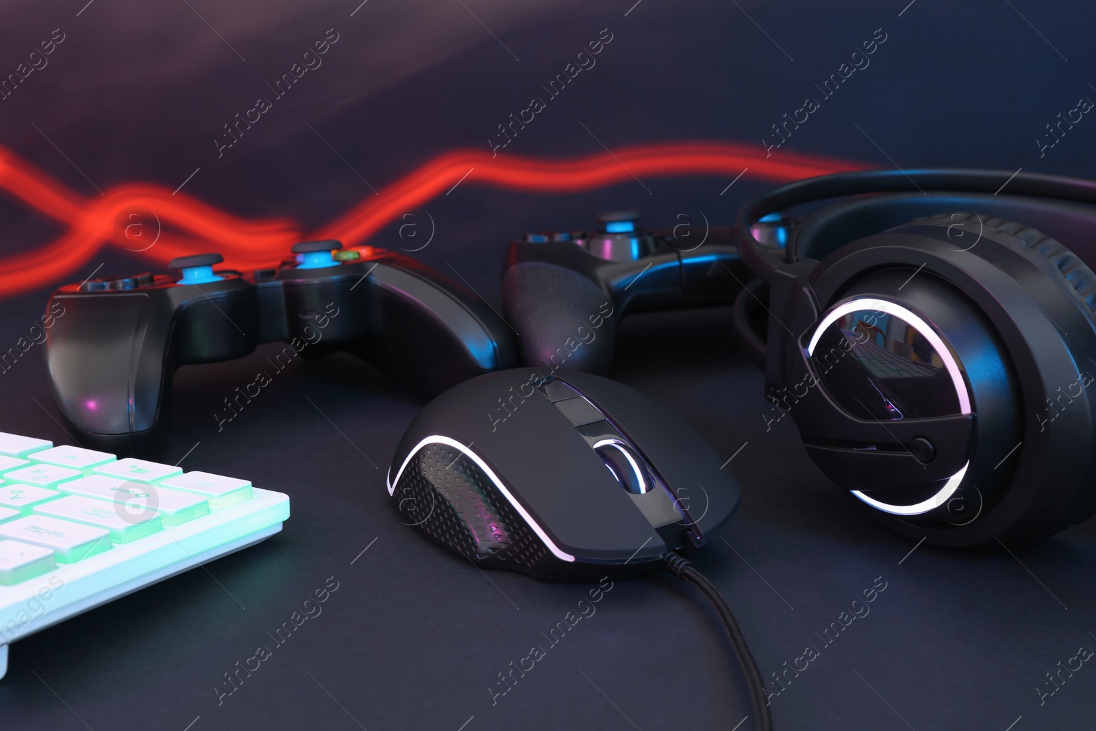 Photo of Computer mouse, headset, RGB keyboard and game controllers on black background, closeup