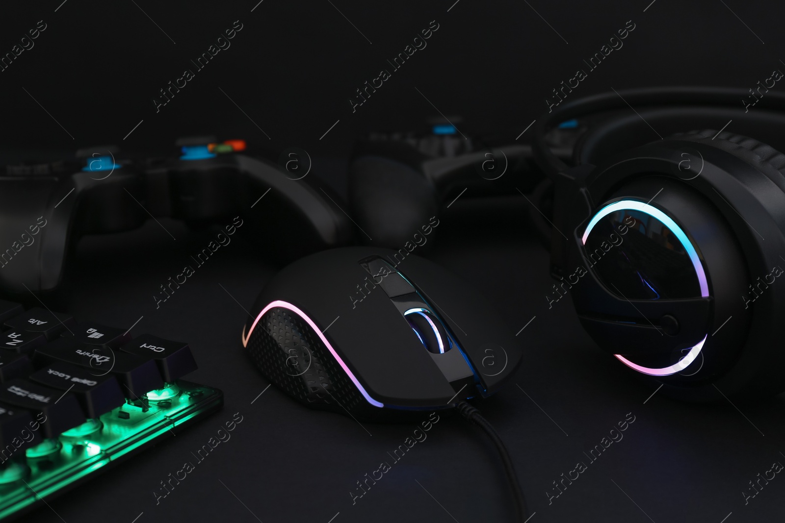 Photo of Computer mouse, headset, RGB keyboard and game controllers on black background, closeup