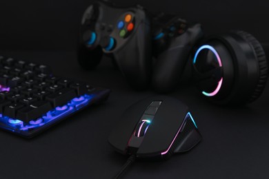 Computer mouse, headset, RGB keyboard and game controllers on black background, closeup