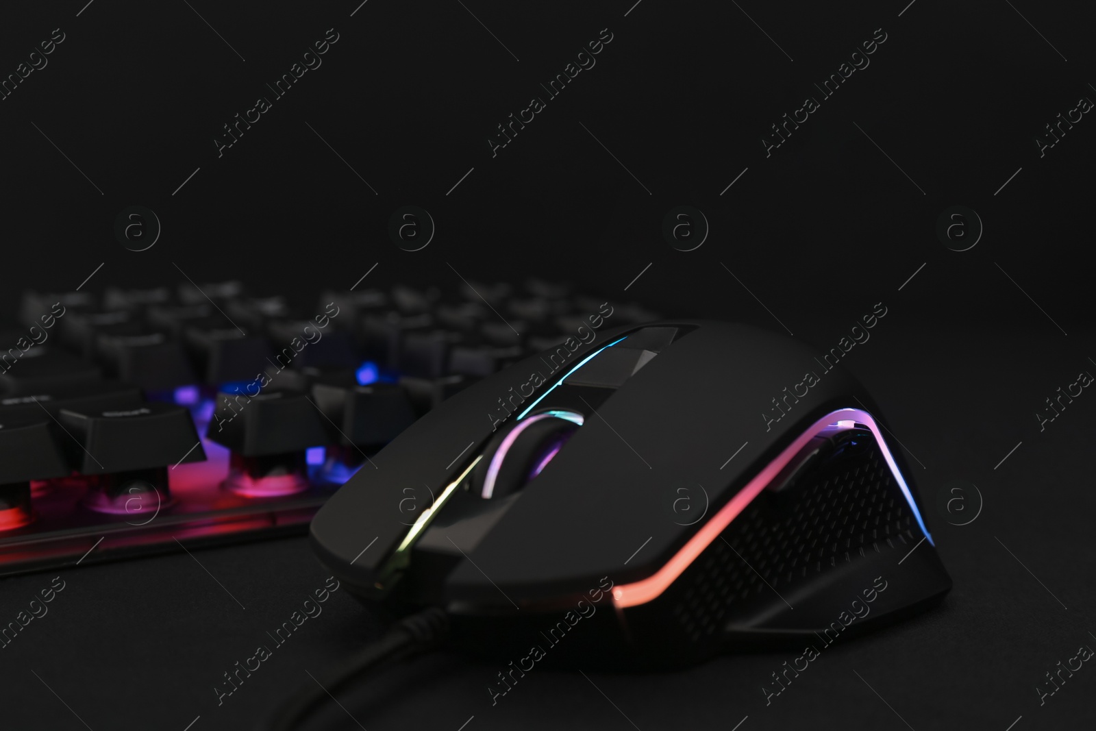 Photo of Computer mouse and RGB keyboard on black background, closeup