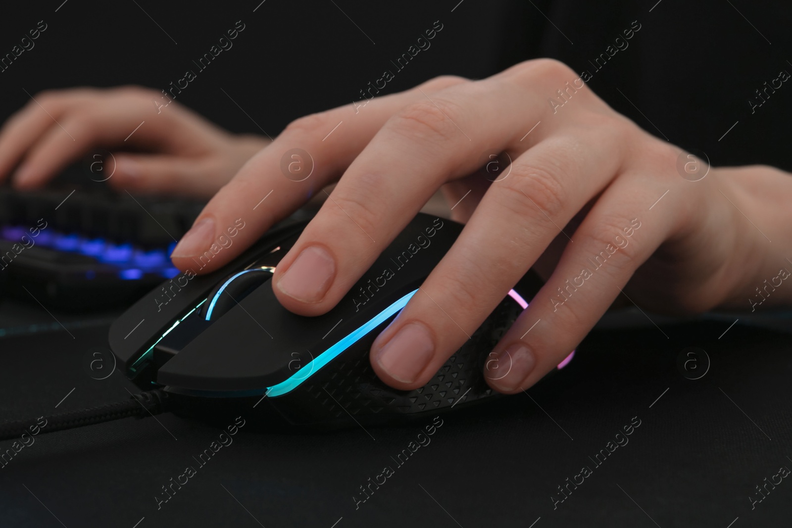 Photo of Gamer using modern wired computer mouse at dark table, closeup