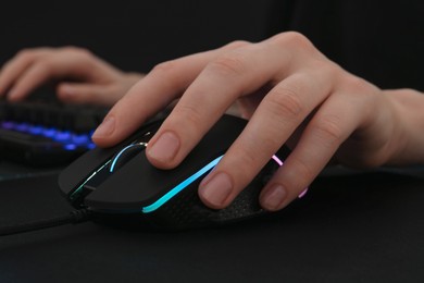 Gamer using modern wired computer mouse at dark table, closeup