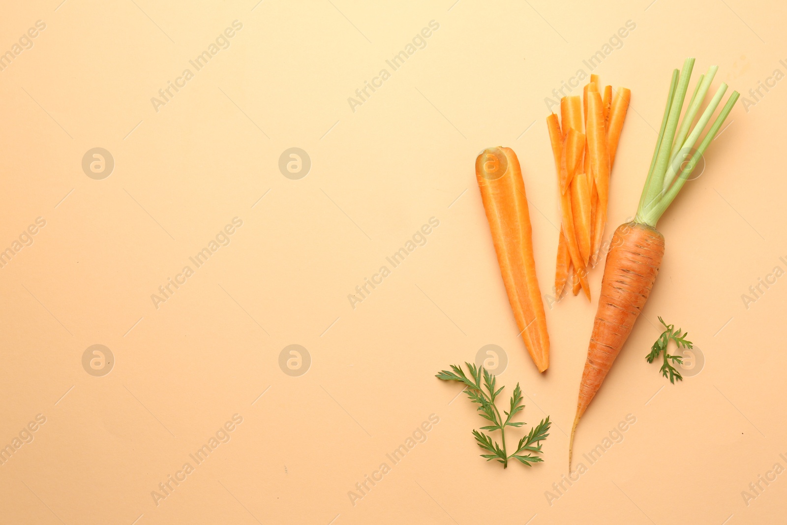 Photo of Whole and cut carrots with green leaves on pale orange background, flat lay. Space for text