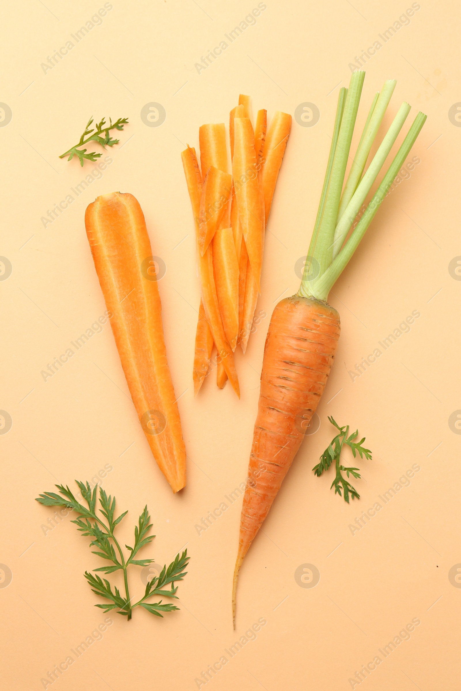 Photo of Whole and cut carrots with green leaves on pale orange background, flat lay