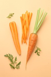 Whole and cut carrots with green leaves on pale orange background, flat lay