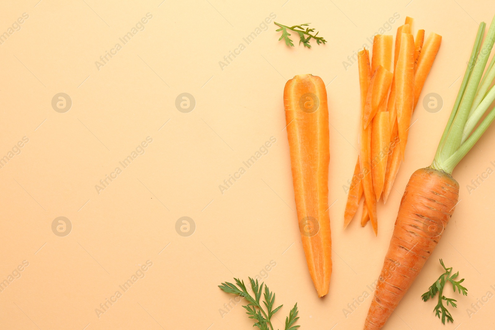 Photo of Whole and cut carrots with green leaves on pale orange background, flat lay. Space for text