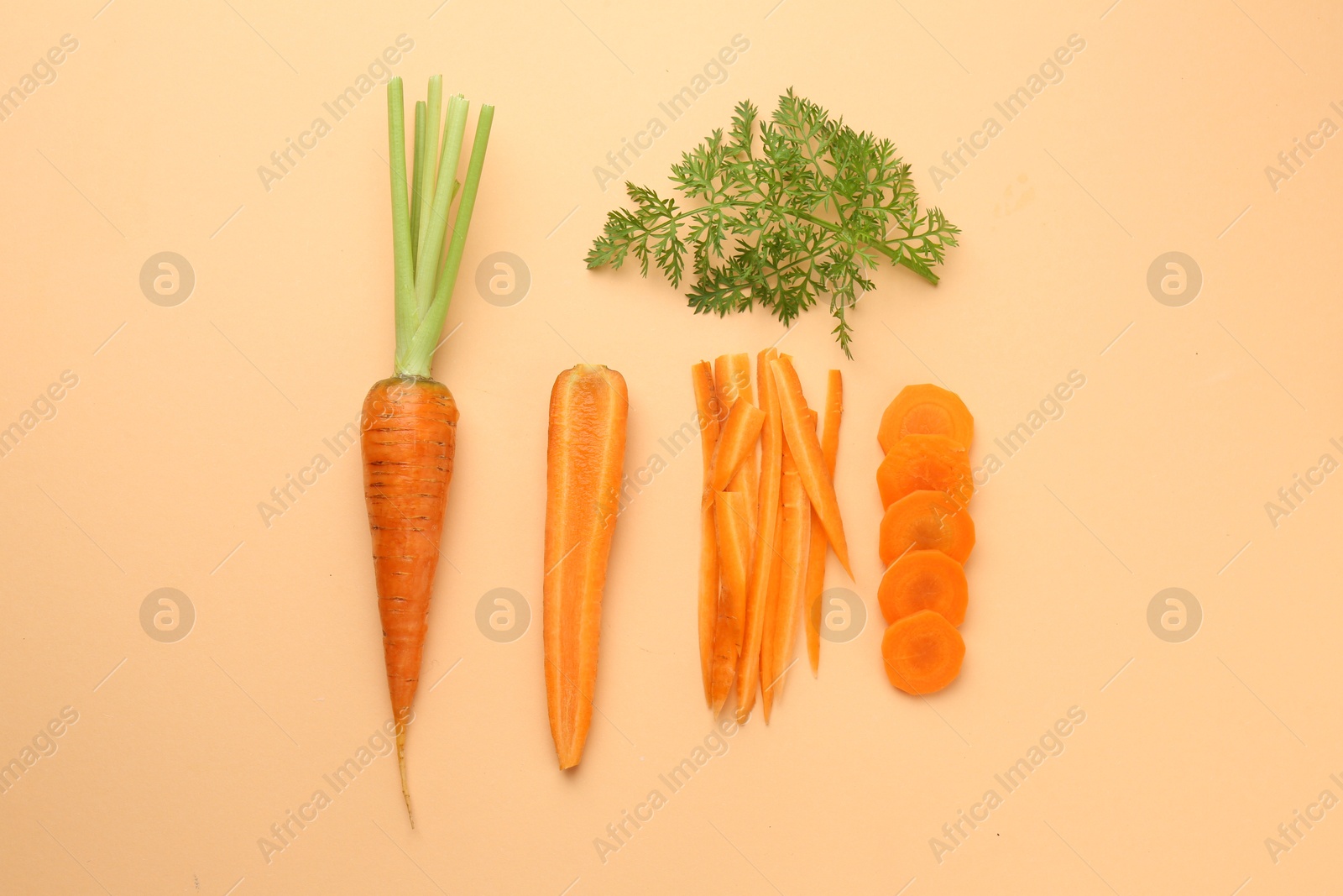 Photo of Whole and cut carrots with green leaf on pale orange background, flat lay