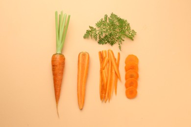 Photo of Whole and cut carrots with green leaf on pale orange background, flat lay