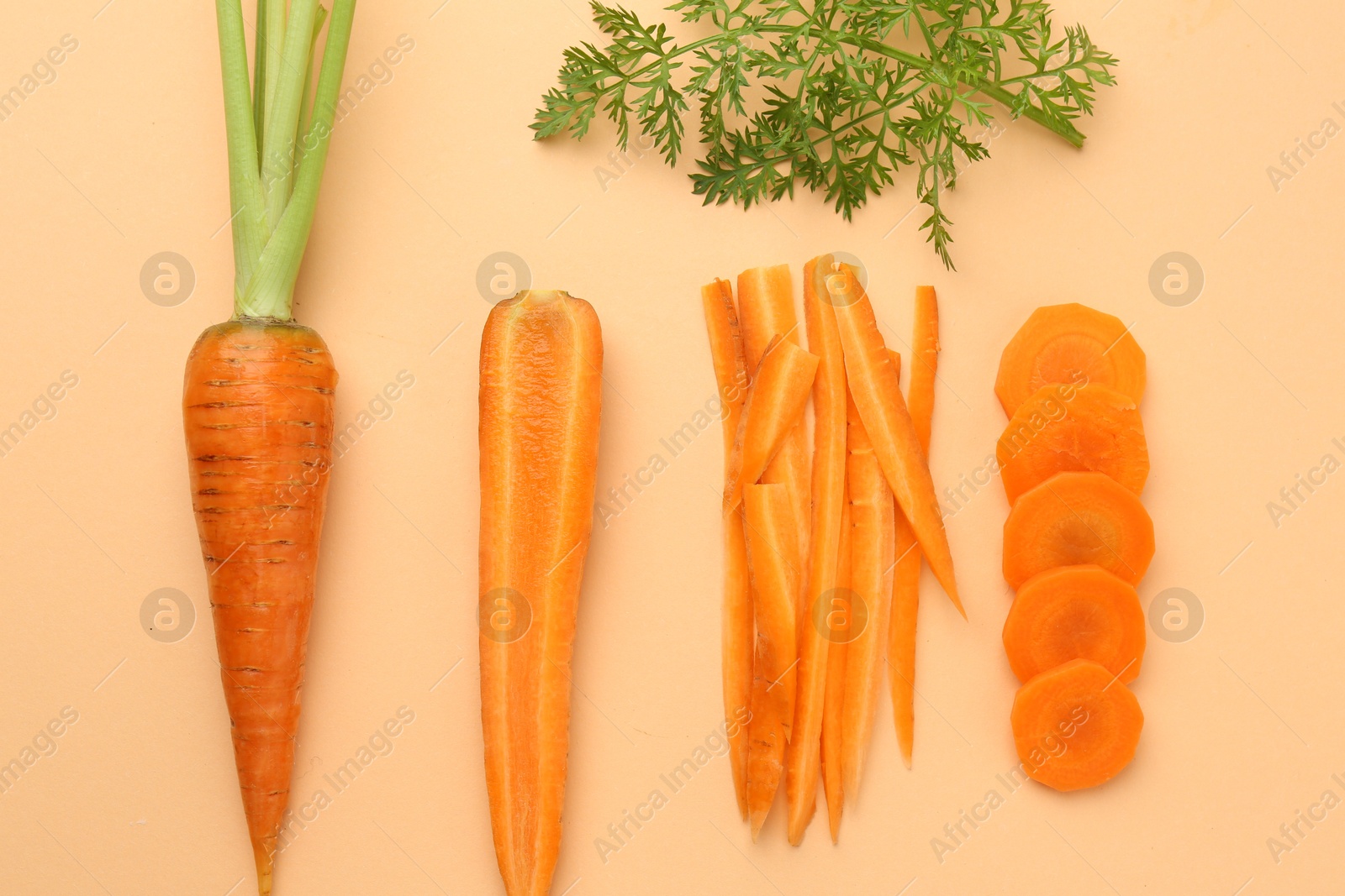 Photo of Whole and cut carrots with green leaf on pale orange background, flat lay