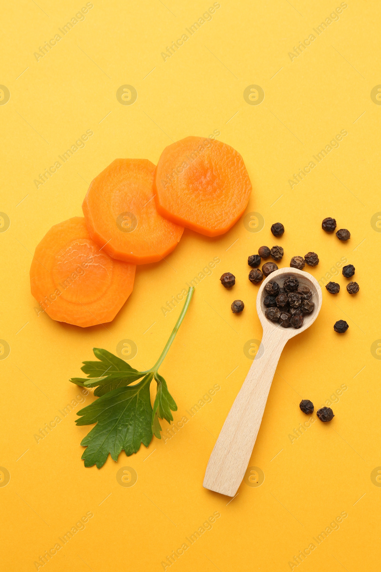 Photo of Slices of fresh ripe carrot, spices and spoon on yellow background, flat lay