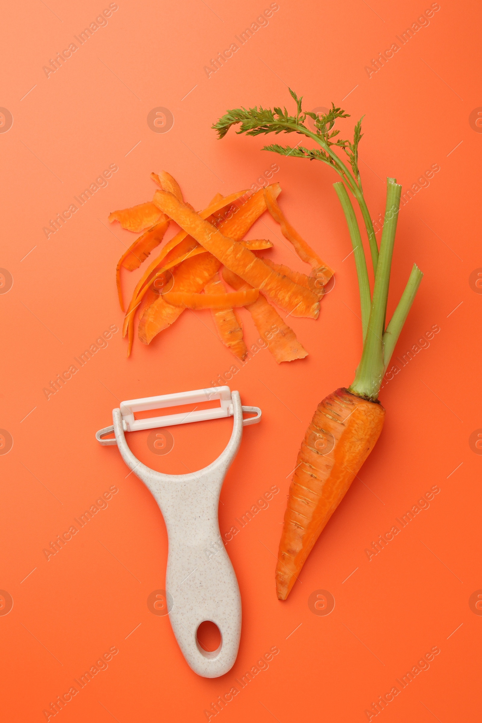 Photo of Fresh carrot, vegetable peeler and peels on orange background, flat lay