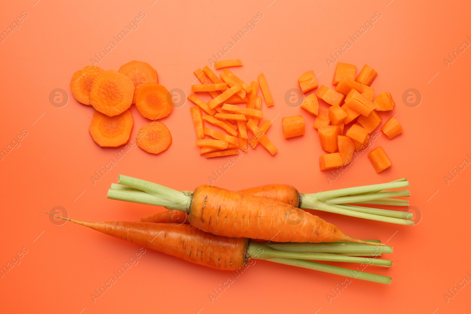 Photo of Whole and cut carrots on orange background, flat lay.