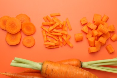 Whole and cut carrots on orange background, flat lay.