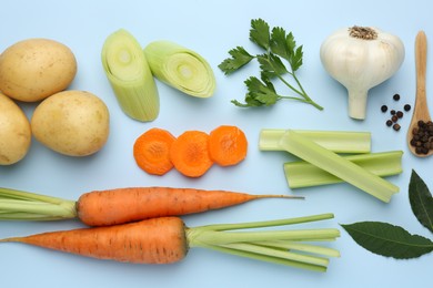 Photo of Fresh ripe carrots, vegetables, spices and spoon on light blue background, flat lay