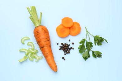 Photo of Fresh ripe carrots, pieces of celery and spices on light blue background, flat lay