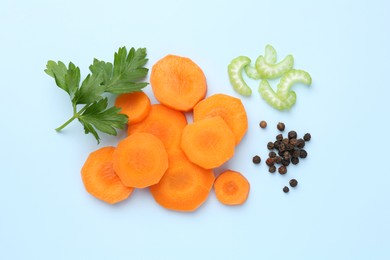 Photo of Slices of fresh ripe carrot, celery and spices on light blue background, flat lay