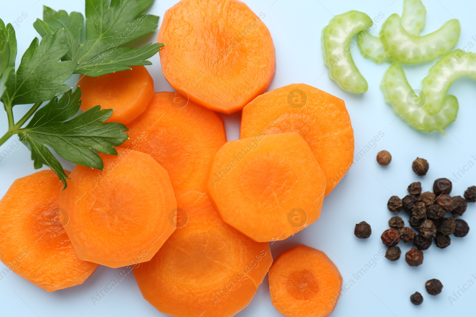 Photo of Slices of fresh ripe carrot, celery and spices on light blue background, flat lay