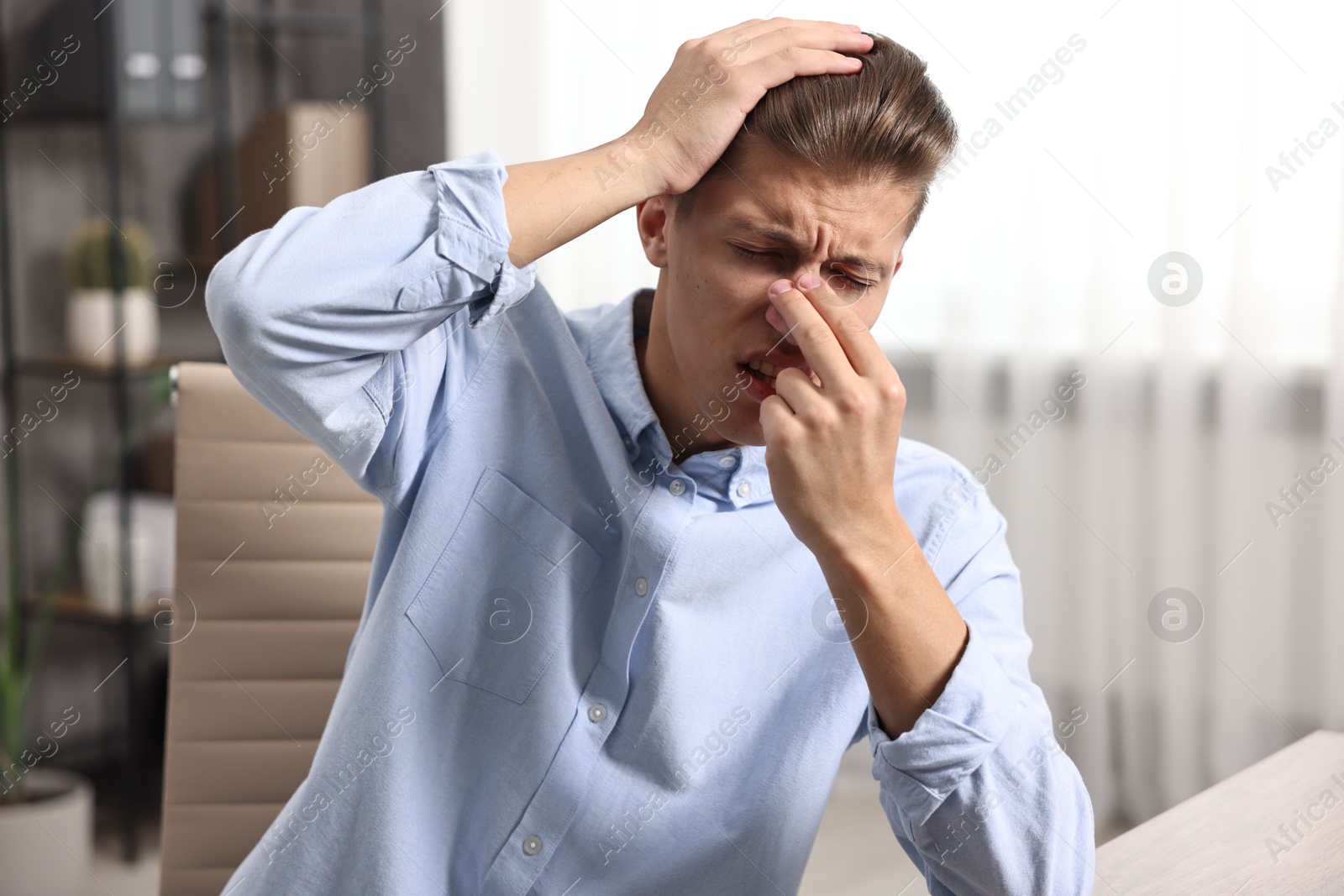 Photo of Young man with tissue suffering from sinusitis at wooden table indoors