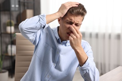 Photo of Young man with tissue suffering from sinusitis at wooden table indoors