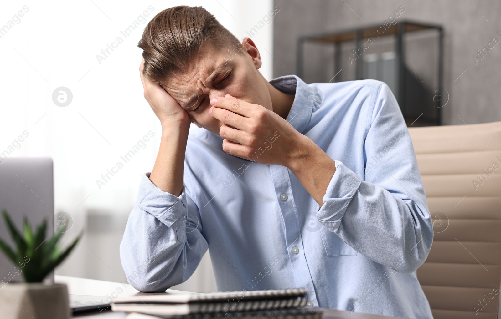 Photo of Young man suffering from sinusitis at wooden table indoors