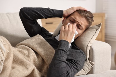 Photo of Young man with tissue suffering from sinusitis and lying in bed at home