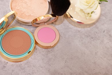 Photo of Bronzer, powder, blusher, brush and rose flower on grey textured table, above view