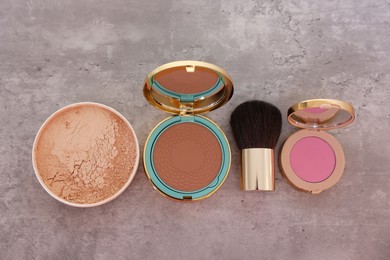 Bronzer, powder, blusher and brush on grey textured table, flat lay