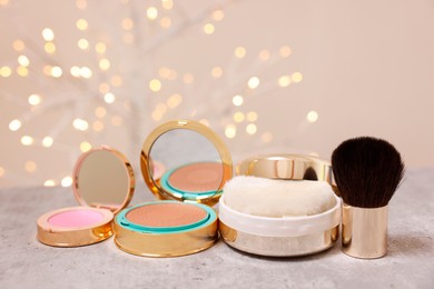 Photo of Bronzer, powder, blusher and brush on grey textured table against blurred lights, closeup