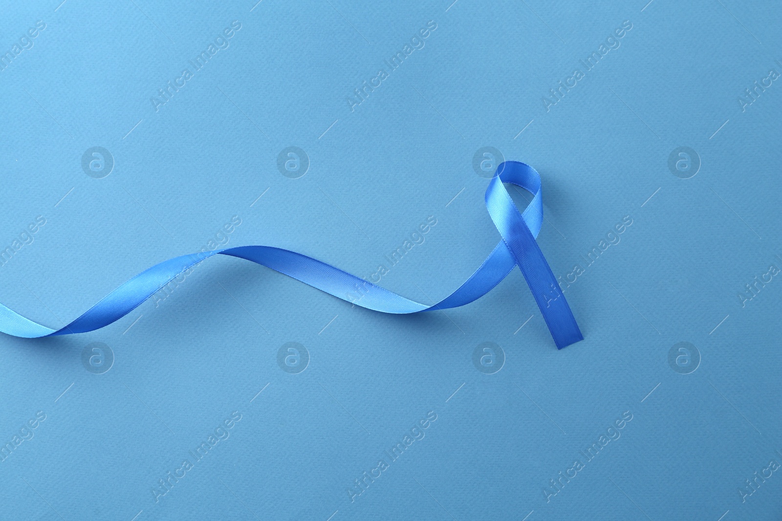 Photo of Blue awareness ribbon on color background, top view