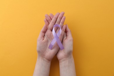 Photo of Woman with violet awareness ribbon on orange background, top view