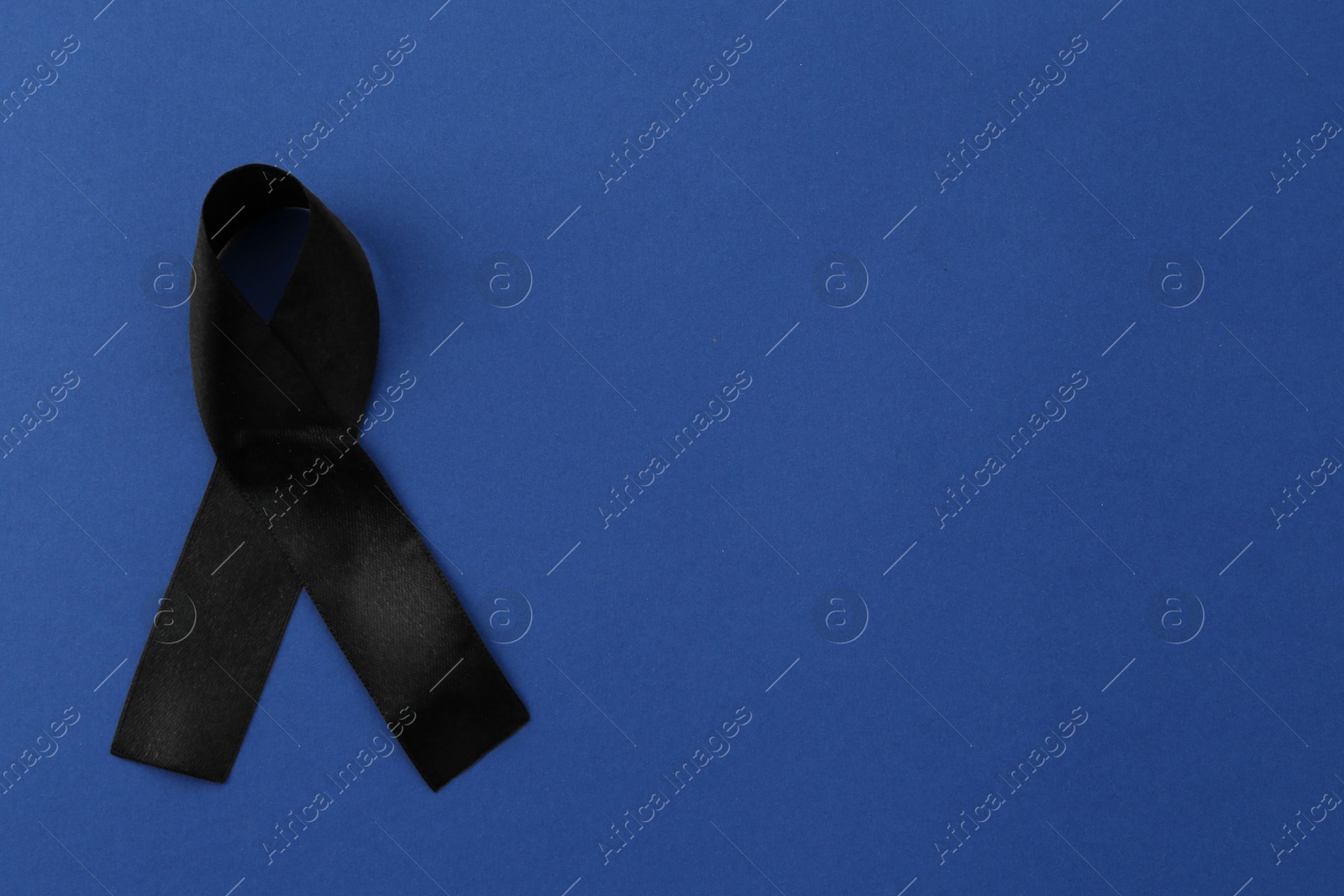 Photo of Black awareness ribbon on blue background, top view. Space for text