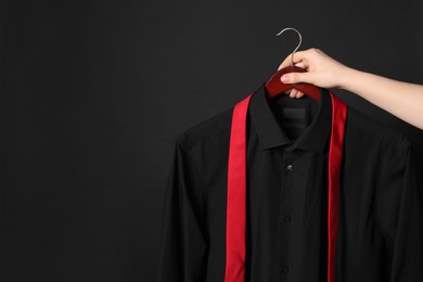 Photo of Woman holding hanger with shirt and necktie on black background, space for text