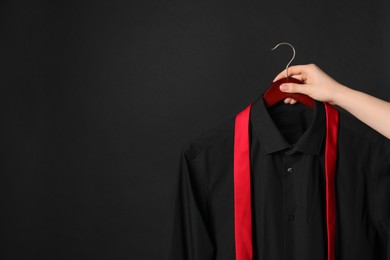 Photo of Woman holding hanger with shirt and necktie on black background, space for text