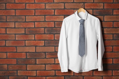 Photo of Hanger with white shirt and striped necktie on red brick wall, space for text