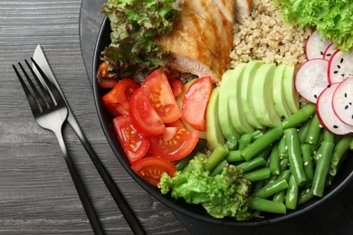 Photo of Healthy meal. Tasty products in bowl and cutlery on black wooden table, top view