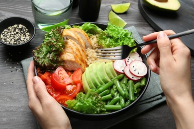 Healthy meal. Woman with bowl of tasty products at black wooden table, closeup