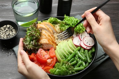 Photo of Healthy meal. Woman with bowl of tasty products at black wooden table, closeup