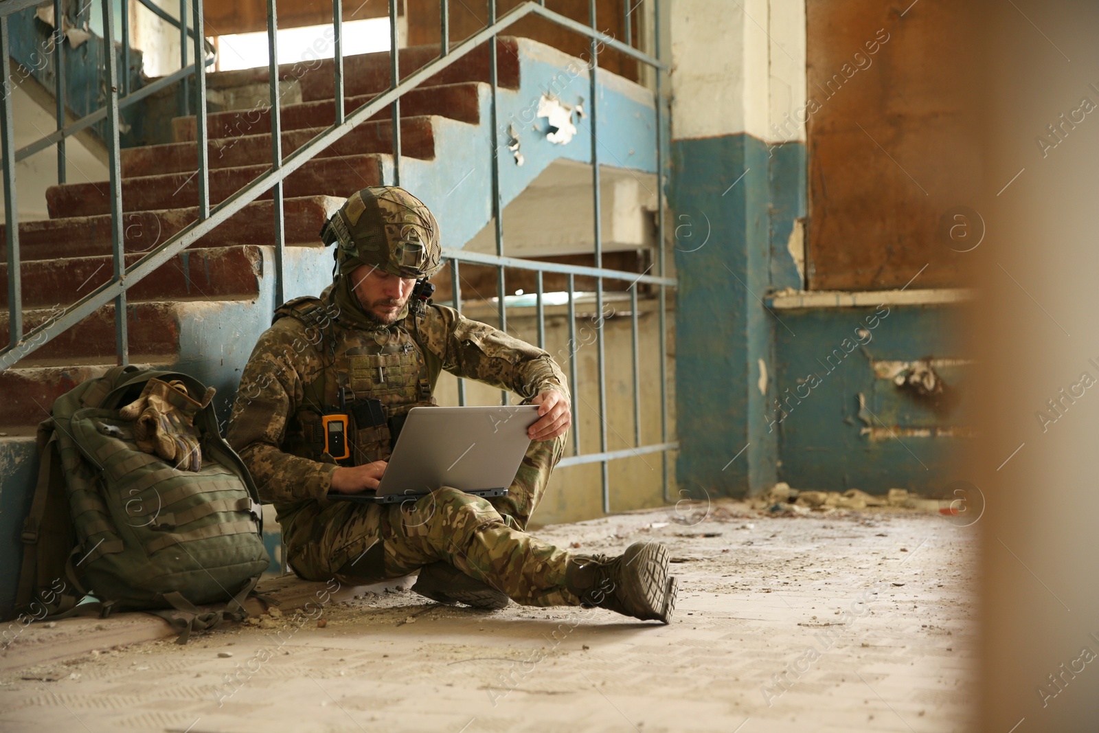 Photo of Military mission. Soldier in uniform using laptop inside abandoned building