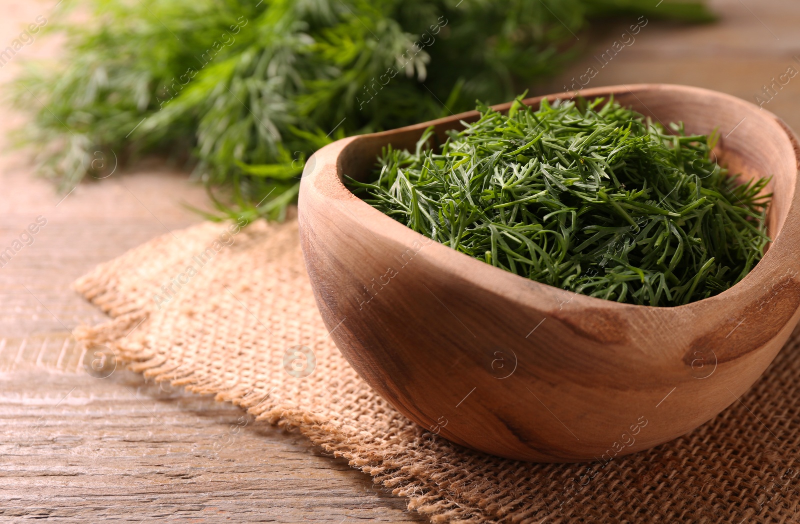 Photo of Fresh cut dill in bowl on wooden table, closeup. Space for text