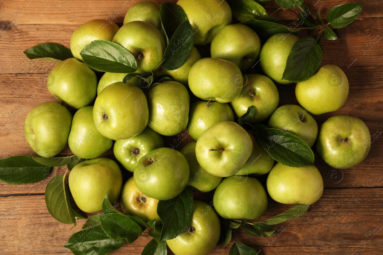 Photo of Ripe green apples with leaves on wooden table, flat lay