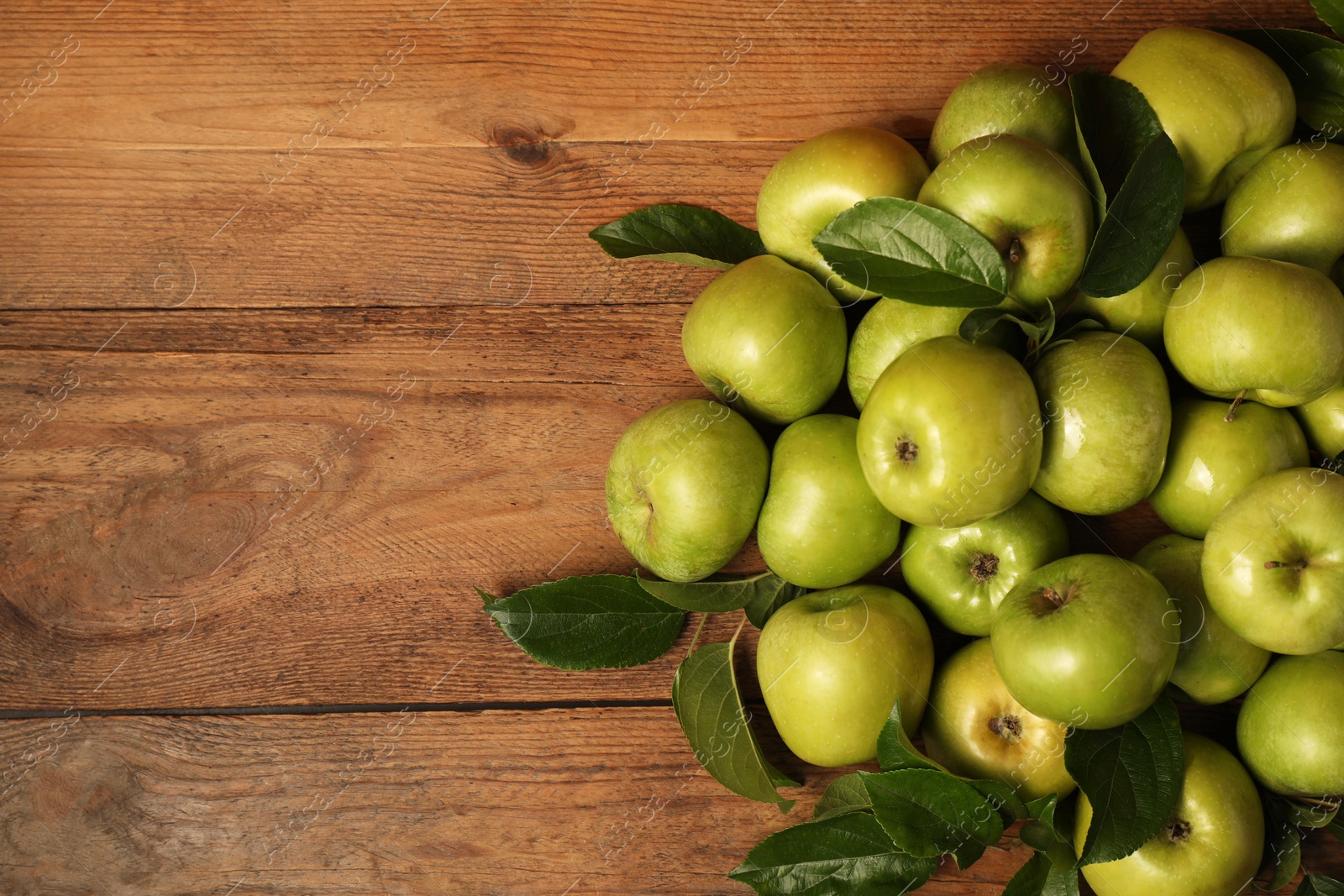 Photo of Ripe green apples with leaves on wooden table, flat lay. Space for text