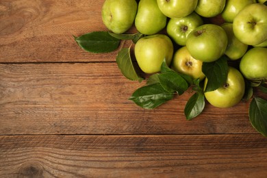 Photo of Ripe green apples with leaves on wooden table, flat lay. Space for text